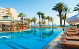 Großer Außenpool mit zahlreichen Liegen, Palmen und einer stilvollen Poolbar direkt am Wasser.