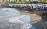 Eleganter Strandabschnitt mit weißen Baldachinliegen und blauen Polstern direkt am Wasser – ideal für erholsame Stunden mit Meeresrauschen.