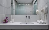 Modernes Badezimmer in elegantem Marmor-Design mit großer Dusche, breitem Spiegel und stilvollen Details – ideal für entspannte Wohlfühlmomente während des Urlaubs.