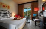 Gemütliches Hotelzimmer mit romantischem Flair, einem großen Doppelbett mit dekorativem Schmiedeeisen-Kopfteil, warmen Farbtönen, stilvollen Lampen und Zugang zum Balkon mit Blick ins Grüne.