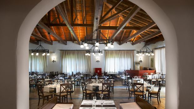 Traditionell eingerichtetes Restaurant mit rustikalem Charme, gemütlichen Holzmöbeln, weiß eingedeckten Tischen und einer offenen Holzbalkendecke – warme Beleuchtung sorgt für ein einladendes Ambiente.