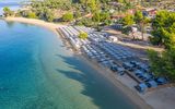 Breiter Sandstrand mit glasklarem Wasser und zahlreichen Sonnenliegen mit Schirmen, umgeben von grüner Natur und kleinen Hotelanlagen – perfekter Ort für entspannte Badetage.