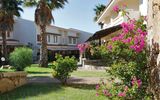 Gepflegte Gartenanlage mit blühenden Bougainvilleen, Palmen und mediterraner Architektur – einladende Umgebung für einen entspannten Aufenthalt.