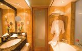 Elegantes Badezimmer in warmen Marmortönen mit großer Spiegelwand, Badewanne, Granitwaschtisch und gemütlichem Bademantel.