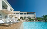 Einladender Außenpool mit hellen Liegen und Sonnenschirmen vor einem mediterranen Hotelgebäude – perfekter Ort zum Entspannen unter strahlend blauem Himmel.