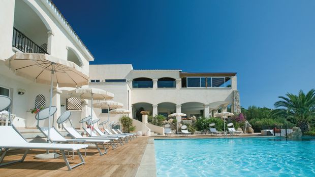 Einladender Außenpool mit hellen Liegen und Sonnenschirmen vor einem mediterranen Hotelgebäude – perfekter Ort zum Entspannen unter strahlend blauem Himmel.