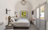 Helles und modern eingerichtetes Doppelzimmer mit schlichter Eleganz, gemütlichem Bett, stylischen Lampen und Blick auf grüne Pinien durch das Fenster.