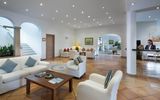 Helle Hotel-Lobby mit freundlicher Rezeption, gemütlichen Sitzgruppen in Weiß und mediterranem Fliesenboden, stilvoll dekoriert mit Pflanzen und Kunstwerken – ideal zum Entspannen beim Check-in.