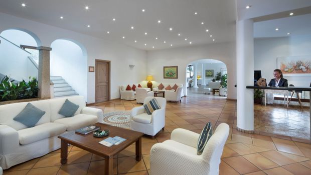 Helle Hotel-Lobby mit freundlicher Rezeption, gemütlichen Sitzgruppen in Weiß und mediterranem Fliesenboden, stilvoll dekoriert mit Pflanzen und Kunstwerken – ideal zum Entspannen beim Check-in.