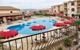 Charmante Hotelanlage im mediterranen Stil mit großem Außenpool, umgeben von Sonnenliegen und roten Sonnenschirmen – ideal für entspannte Urlaubstage.