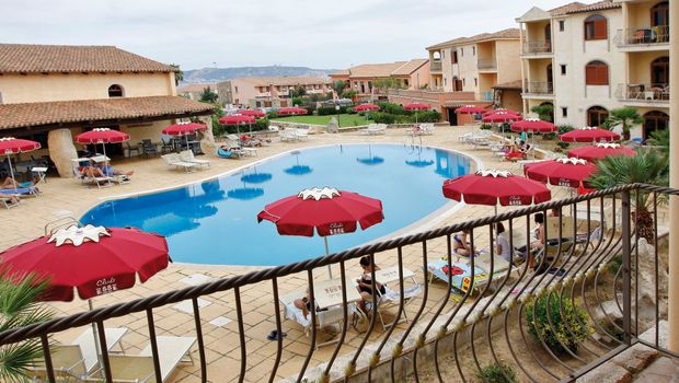 Charmante Hotelanlage im mediterranen Stil mit großem Außenpool, umgeben von Sonnenliegen und roten Sonnenschirmen – ideal für entspannte Urlaubstage.