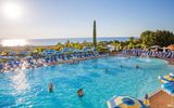 Großer Außenpool mit Wasserspiel und vielen blauen Sonnenliegen und Schirmen – traumhafter Blick aufs Meer und ideale Bedingungen für entspannte Badetage unter der Sonne.