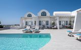 Modernes Boutique-Hotel im kykladischen Stil mit weißer Fassade, blauen Fensterläden und Poolterrasse mit Liegen – klare Architektur und mediterranes Flair unter strahlend blauem Himmel.