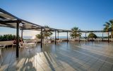 Großzügige Terrasse mit weißen Tischen und Stühlen unter Pergolen – ideal zum Speisen oder Entspannen mit Panoramablick auf das Meer und die untergehende Sonne.