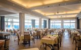 Helles Restaurant mit Meerblick, großen Panoramafenstern und freundlich gedeckten Tischen.