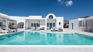 Boutique-Hotel im kykladischen Stil mit strahlend weißer Architektur, türkisfarbenen Fensterläden und großzügigem Poolbereich – stilvolles Design in ruhiger Lage unter klarem, blauem Himmel.