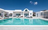 Boutique-Hotel im kykladischen Stil mit strahlend weißer Architektur, türkisfarbenen Fensterläden und großzügigem Poolbereich – stilvolles Design in ruhiger Lage unter klarem, blauem Himmel.